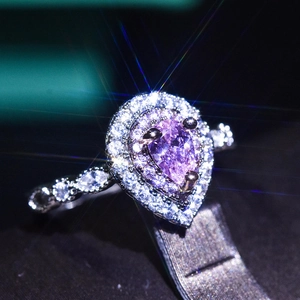 Macro detail of platinum-plated ring featuring pear-cut purple gemstone and halo diamonds