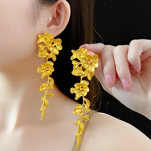 Détail des boucles d'oreilles fleuries en or mat avec pampilles et motifs de feuilles