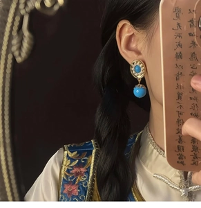 Model wearing vintage style blue bead earrings with gold engraved discs in close-up shot