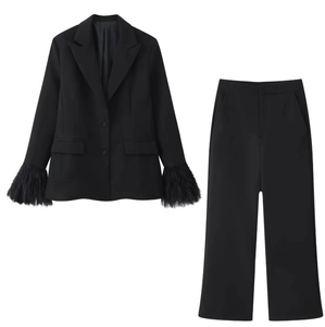Dettaglio di un blazer nero con polsini in piuma e pantaloni sartoriali coordinati da donna