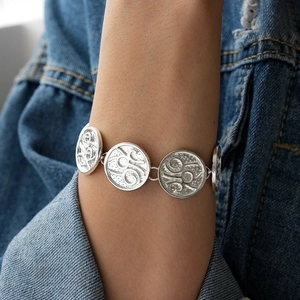 Close-up of a silver textured round relief bracelet worn on a wrist over denim fabric