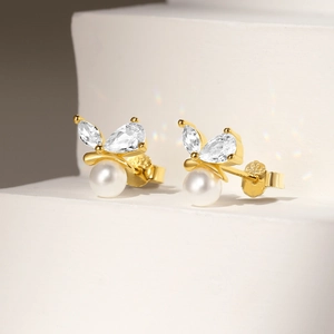 Detailed macro of gold butterfly earrings with teardrop zircon and white pearl accents