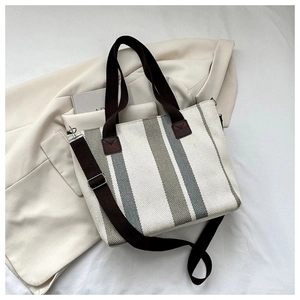 Detail view of striped canvas tote bag with wide brown straps on a beige blazer