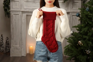 Close-up of red cable knit Christmas stocking held by a model in a festive room