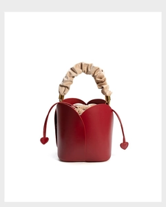 Detail of red petal-shaped bucket bag with beige ruched handle and heart charms