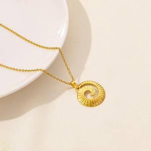 Detail of a golden spiral vortex pendant on a fine chain over a white ceramic dish
