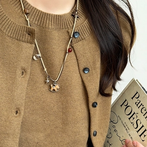 Close-up of a vintage wood rocking horse pendant on a brown woven sweater chain