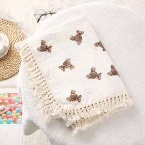 Detail of soft cream cotton baby blanket featuring brown bear prints and fringe edges