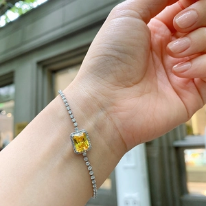 Detailed view of silver bracelet with yellow square gemstone worn on a wrist outdoors