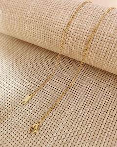 Detail of golden stainless steel chain featuring a lobster clasp on woven fabric