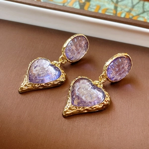 Macro detail of vintage gold textured oval earrings with purple heart charms