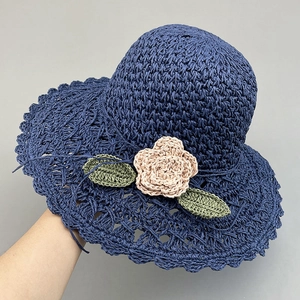 Close-up of hand-woven navy straw hat featuring pink crochet flower and green leaves