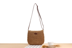 Detail of hand-woven paper rope crossbody bag with leather strap on a rustic table