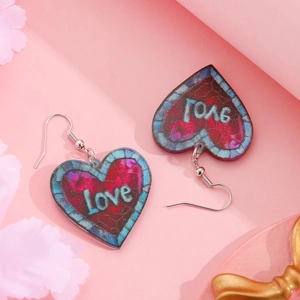 Macro detail of heart-shaped Love graffiti earrings on decorative pink floral background