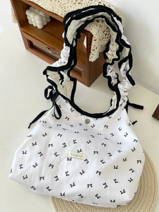 White tote bag with floral bow print and ruffled shoulder straps in a cozy home setting