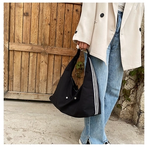 Detail of black nylon tote bag featuring three white stripes on a textured street setting