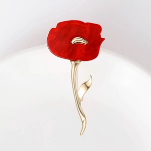 Detail of red enamel poppy flower brooch with golden metal leaves on a white background