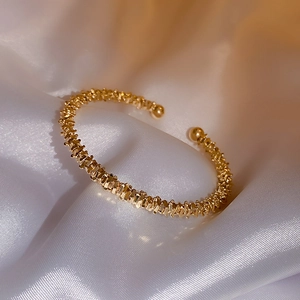 Close-up of golden geometric textured open bracelet on white silk satin fabric