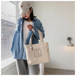 Detail of beige corduroy tote bag featuring a cartoon rabbit embroidery and plush cow charm
