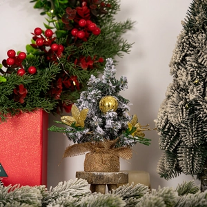 Detailed view of mini snowy Christmas tree with golden ornaments and burlap base