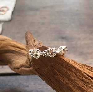Detailed view of 925 sterling silver ring with hollow heart-shaped chain design on dark wood