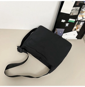 Detail of black nylon messenger bag featuring adjustable strap and front zipper pocket