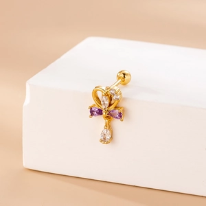 Detail of gold piercing stud featuring cross heart design and purple drop stone