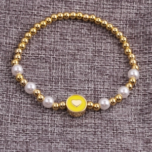 Detailed view of a gold-plated beaded bracelet with white pearls and a heart pendant