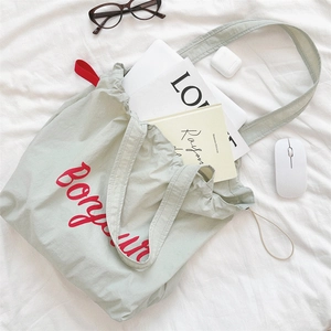 Detail of red Bonjour embroidery on light green drawstring canvas tote bag with props