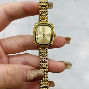 Dettaglio dell'orologio rettangolare dorato con cinturino a treccia e numero romano XII
