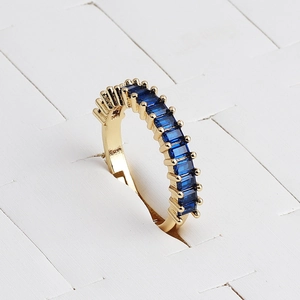 Close-up of gold ring with blue rectangular zircons on a textured white display
