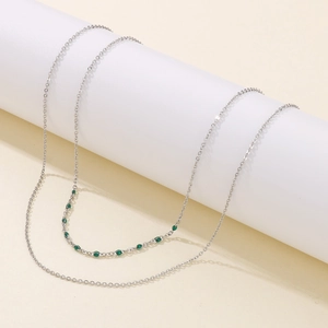 Détail d'un collier double épaisseur en acier argenté avec perles vertes sur support