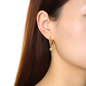 Close-up of a gold stainless steel hoop earring with a dangling star charm on ear