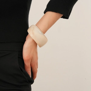 Detail of wide cream resin bangle with marble texture worn on model's wrist