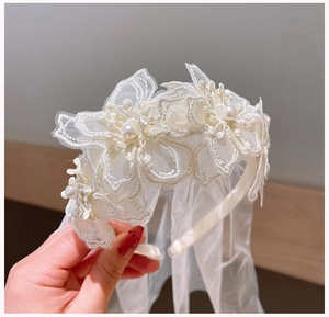 Detail of white lace flower headband with pearls and long bridal veil for girls