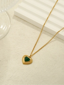 Close-up of a gold heart necklace featuring a deep green gemstone and beaded edges