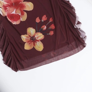 Detail van een wijnrode mesh jurk met oranje bloemenprint en ruches aan de zoom