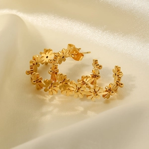 Detalle de pendientes de flores doradas en forma de C de acero sobre tela de seda beige