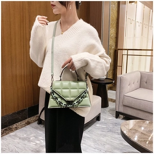 Detail view of a green quilted geometric shoulder bag with gold chain and leather strap