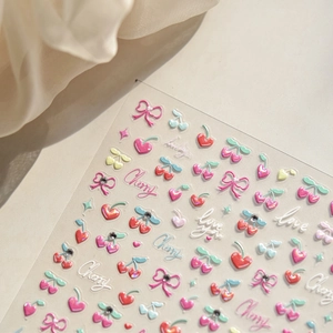 Macro shot of 3D nail stickers featuring cherry, heart, and bow patterns on fabric