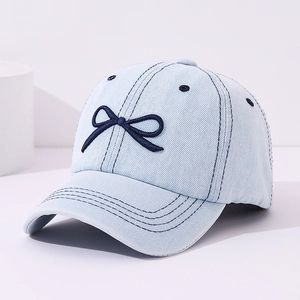 Detail of light blue denim cap featuring dark blue bow embroidery and twill texture