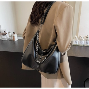 Detail of black PU leather shoulder bag with white stitching and metal chain on model