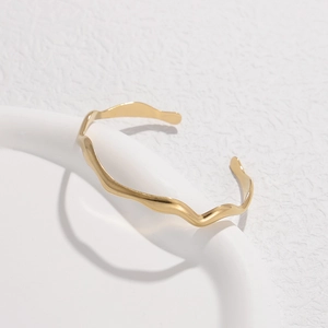 Macro shot of polished gold wave-shaped stainless steel bangle on white ceramic