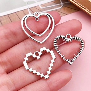 Three vintage silver hollow heart charms in pixelated and thorn styles held in hand