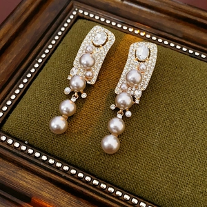 Detailed macro of gold drop earrings with pearls and rhinestones on dark green velvet