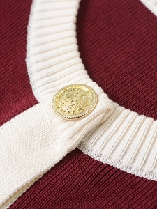 Detail of wine red knit cardigan with cream trim and vintage gold emblem button