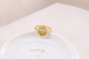 Detailed view of a gold hollow-out ring with small zircon stones on white ceramic tray