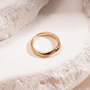 Dettaglio di un anello dorato irregolare con onde su una base di pietra bianca