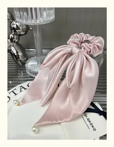 Close-up of pink satin bow scrunchie with long ribbons and elegant pearl pendants