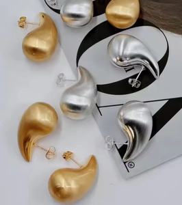 Detailed close-up of teardrop stud earrings in gold and silver finish on white background